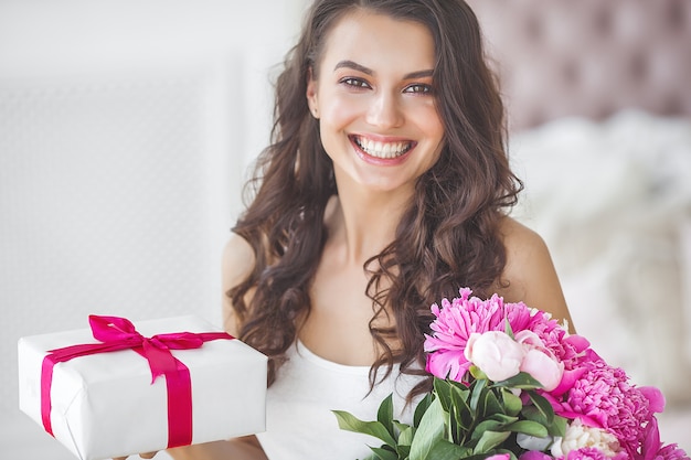 Zeer mooie vrouw met bloemen en cadeau binnenshuis