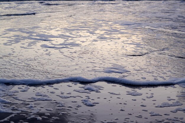 Zeeschuim met iriserende veelkleurige bubbels op het water aan de zandkust