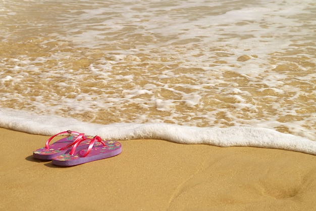 Zeeschuim spettert op het strand een paar sandalen