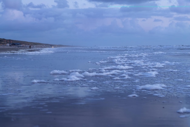 Zeeschuim van de golven aan de kustlijn zandstrand en lage zware wolken bij zonsondergang