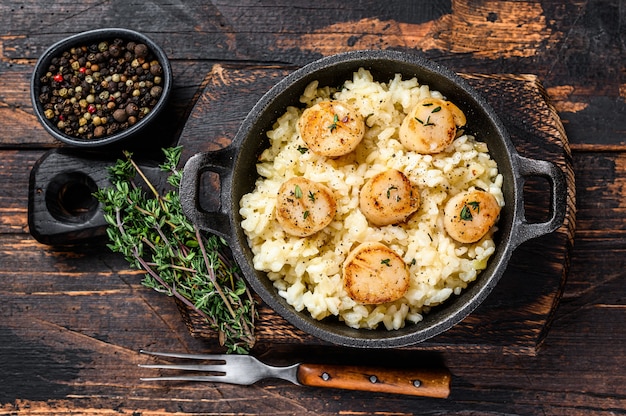 Zeevruchtenrisotto met Sint-jakobsschelpen in een pan. Donkere houten achtergrond. Bovenaanzicht.