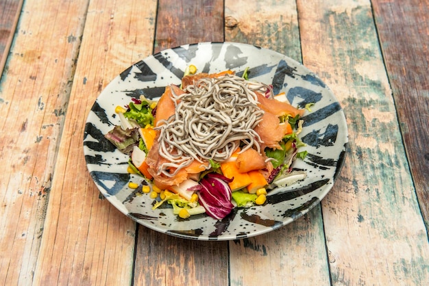 Zeevruchtensalade met gerookte zalm, gehakte surimi baby paling sla in scheuten en suikermaïs op een houten bord