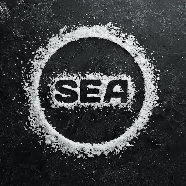 Zeezout met het opschrift SEA Op een zwarte stenen achtergrond Spabehandelingen Bovenaanzicht Vrije ruimte voor uw tekst