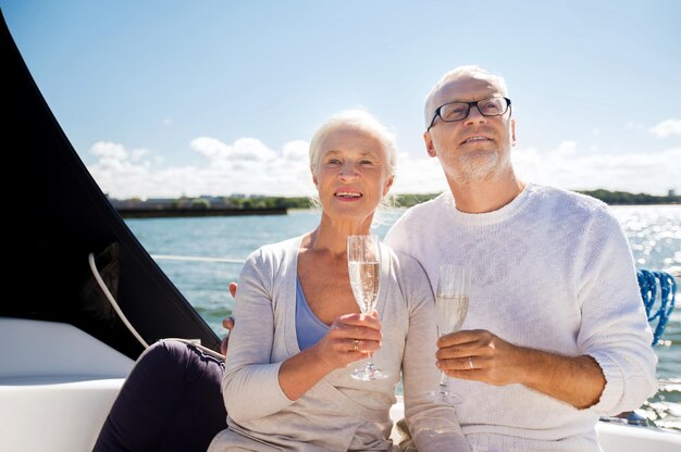 zeilen, leeftijd, reizen, vakanties en mensen concept - gelukkig senior paar met champagneglazen op zeilboot of jachtdek drijvend in zee