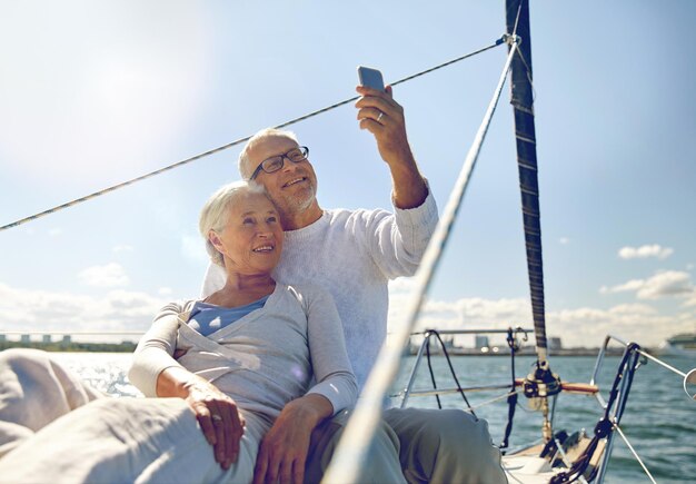 Foto zeilen, technologie, toerisme, reizen en mensen concept - gelukkig senior paar selfie te nemen met smartphone op zeilboot of jachtdek drijvend in zee