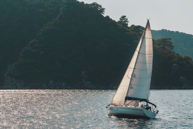 Zeiljacht met witte zeilen op een golvende zee baai op bergen.