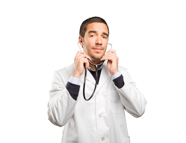 Zekere arts die een stethoscoop gebruikt tegen een witte achtergrond