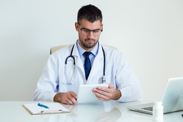 Zekere mannelijke arts die zijn digitale tablet in het bureau gebruiken.