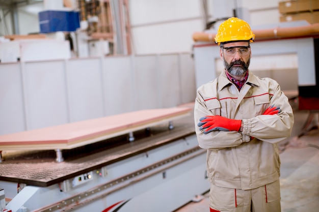 Zekere rijpe mens die zich met gekruiste wapens in de fabriek productie-eenheid met oranje helm