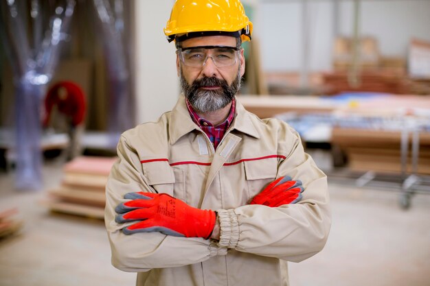 Zekere rijpe mens die zich met gekruiste wapens in de fabriek productie-eenheid met oranje helm