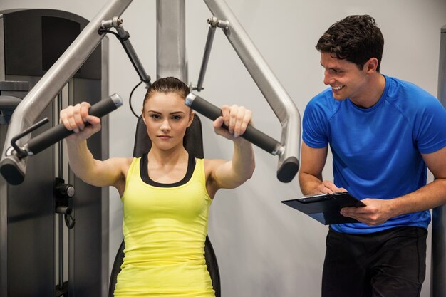 Zekere vrouw die gewichtenmachine met trainer met behulp van