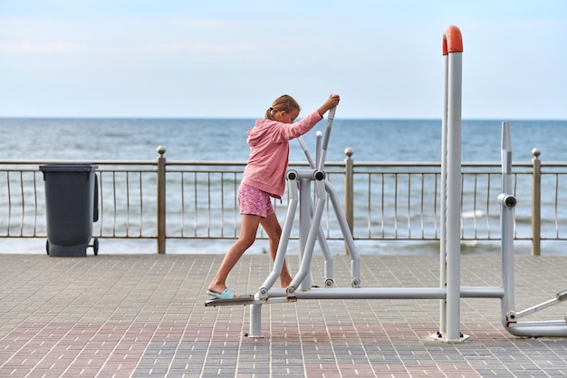 Zelenogradsk, Russia - 07.30.2021 - Young girl in pink clothes using air walker exercise machine, sea background. Girl engaged in fitness, footwork. Outdoor sport exercises and fresh sea air