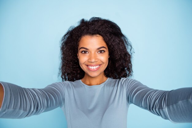 Zelffoto van vrolijke positieve stralende vriendin glimlachend vrolijk nemen selfie in blauwe trui geïsoleerde pastelkleur achtergrond