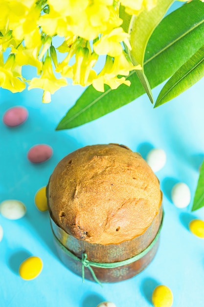 Zelfgebakken cake Panettone, chocolade snoep eieren verspreid over blauw tafelblad met gele bloemen.