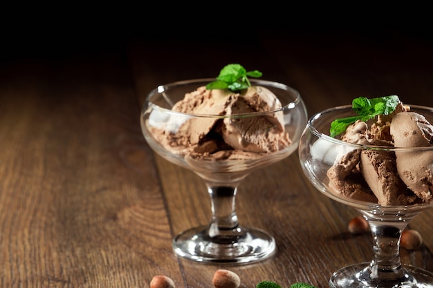 Zelfgemaakt chocoladeroomijs met muntblaadjes, bestrooid met chocolade in een glazen kom op een houten tafel