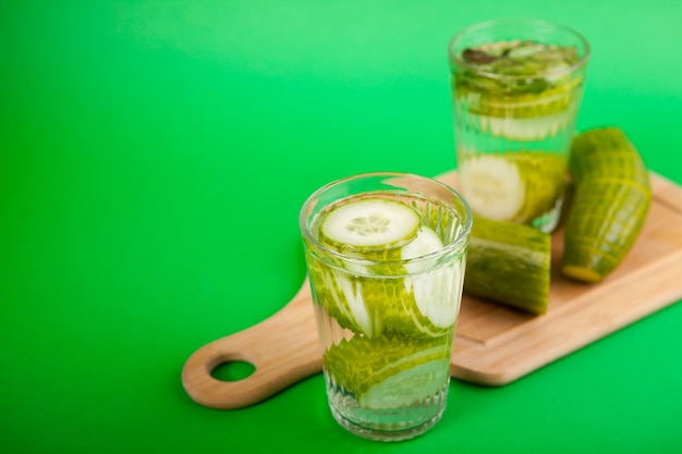 Zelfgemaakt detoxwater van biologische komkommers in een glas tegen een groene achtergrond