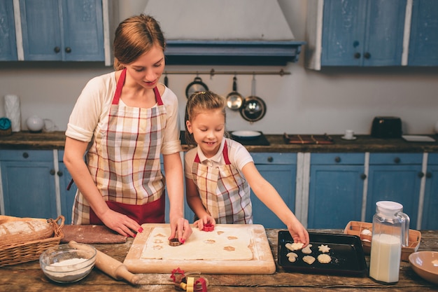 Zelfgemaakt gebak koken. De gelukkige houdende van familie bereidt samen bakkerij voor. Moeder en kind dochter meisje koken koekjes en hebben plezier in de keuken. Rol het deeg uit. Mallen van deeg.