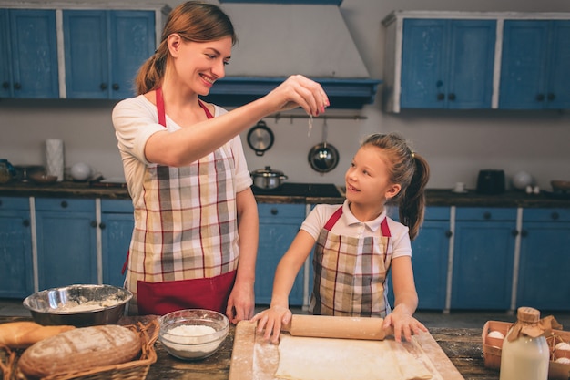 Zelfgemaakt gebak koken. de gelukkige houdende van familie bereidt samen bakkerij voor. moeder en kind dochter meisje koken koekjes en hebben plezier in de keuken. rol het deeg uit.