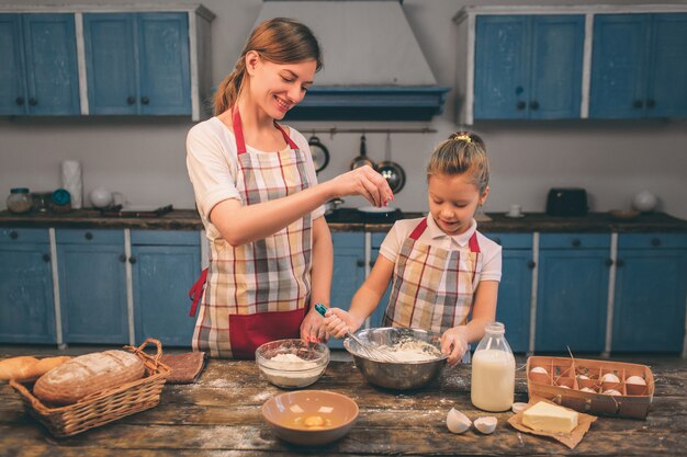 Zelfgemaakt gebak koken. De gelukkige houdende van familie bereidt samen bakkerij voor. Moeder en kind dochter meisje koken koekjes en hebben plezier in de keuken. Rol het deeg uit.