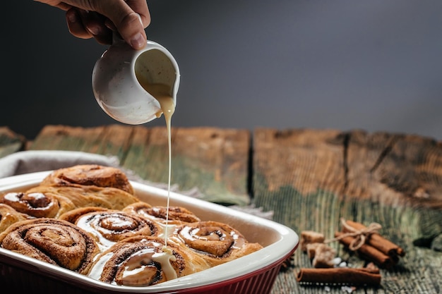 Zelfgemaakt kaneelbroodje Vrouwenhand het verspreiden van vanillesuikerglazuur vers gebakken kaneelbroodjes