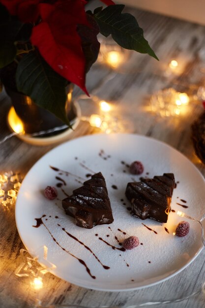 Foto zelfgemaakt kerstboomdessert. vakantie cake met chocolade op keramische plaat met kerstversiering en verlichting als achtergrond. voorbereiden op het nieuwe jaar en kerst