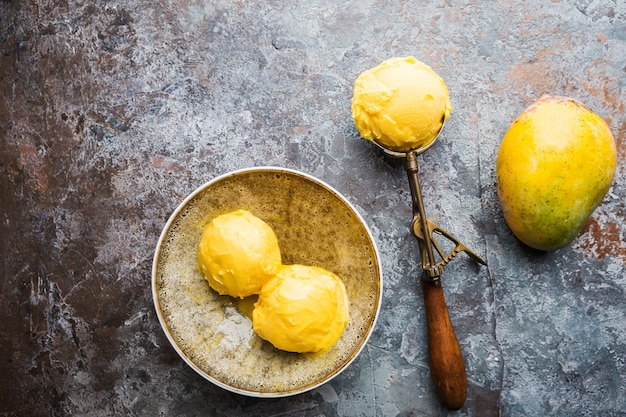 Zelfgemaakt mango-ijs in een kom met vers fruit over donkergrijs