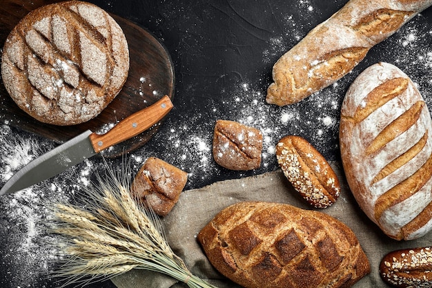 Zelfgemaakt roggebrood bestrooid met bloem en verschillende granen en zaden op een zwarte achtergrond met aartjes van tarwe of rogge en haver