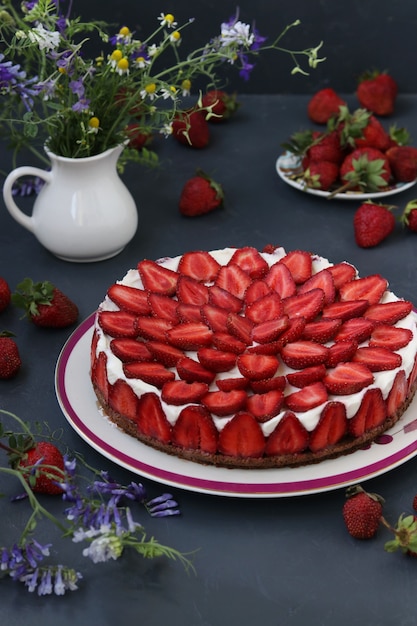 Zelfgemaakte aardbeien cheesecake, versierd met verse aardbeien, op een bord op een donkere achtergrond, verticaal formaat