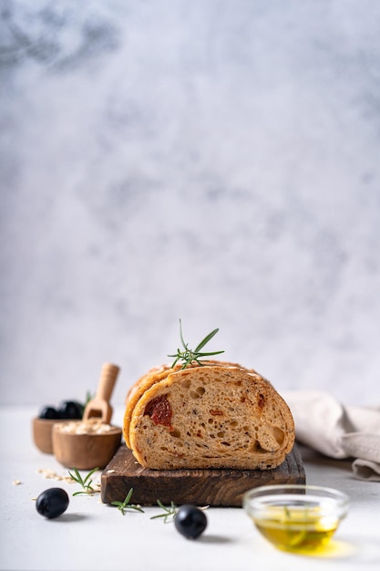 Zelfgemaakte ambachtelijke zuurdesem ciabatta sneetje brood met olijven en rozemarijn op een witte abstracte tafel