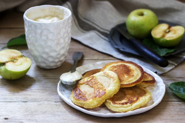 Zelfgemaakte appelbeignets met zure room, koffie en groene appels op een hout