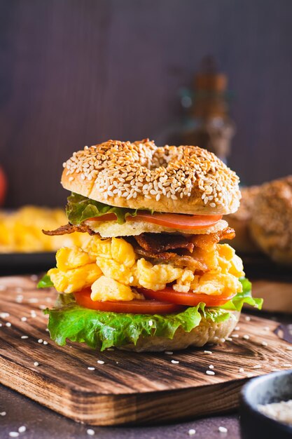 Zelfgemaakte bagel met scramble ei, bacon, kaas, tomaat en sla op een verticaal bord