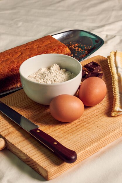 Zelfgemaakte biscuit op een wit tafelkleed met enkele ingrediënten, eieren, chocolade en bloem