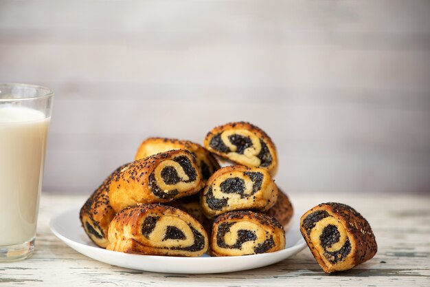 Zelfgemaakte broodjes met maanzaad in witte plaat en kopje melk op lichte houten tafel.