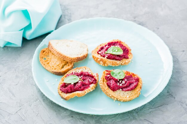 Zelfgemaakte bruschetta met rode biet hummus op kleine gebakken stokbrood toast op een plaat op tafel close-up