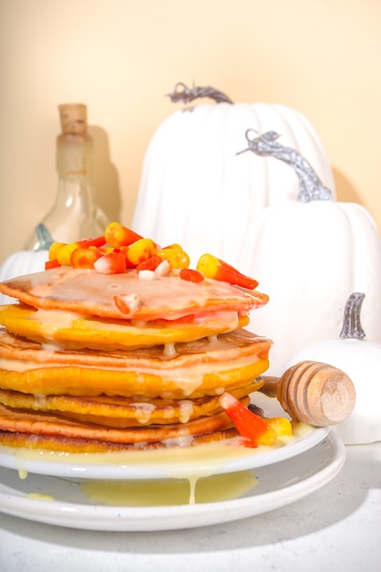 Zelfgemaakte candy corn pannenkoeken. Stapel gele en oranje pannenkoeken met zoete saus en traditionele Halloween-snoepjes met snoepkoord