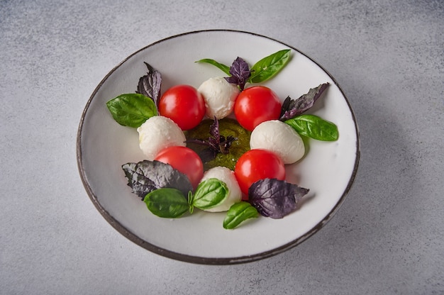 Zelfgemaakte caprese salade met rijpe tomaten, verse basilicum en mozzarella kaas in witte plaat op grijs