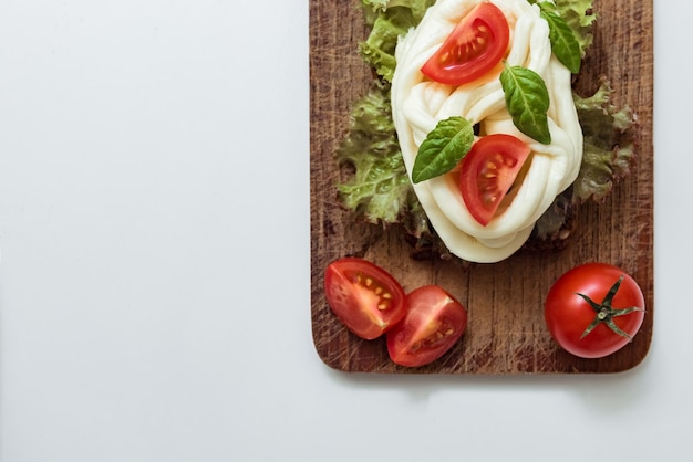 Zelfgemaakte chechil-kaas met verse tomaten, sla en basilicumbladeren op een houten bord, kopieer ruimte