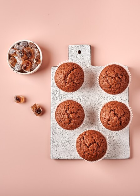 Zelfgemaakte chocolade cupcakes in bakpapier vormen op snijplank op roze poederachtige achtergrond