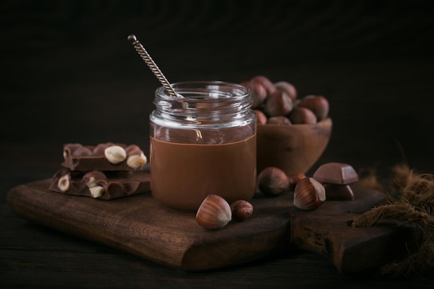 Zelfgemaakte chocolade hazelnoot melk verspreid op glazen pot op donkere houten achtergrond