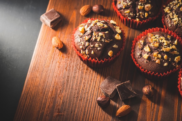Zelfgemaakte chocolade muffins of cupcakes bestrooid met noten op een houten plank