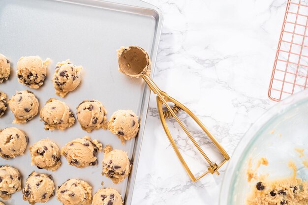 Zelfgemaakte chocoladeschilferkoekjes deeg scoops op een bakplaat.