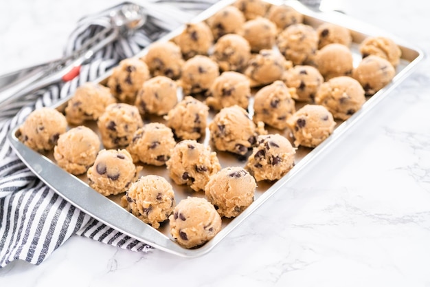 Zelfgemaakte chocoladeschilferkoekjes deeg scoops op een bakplaat.