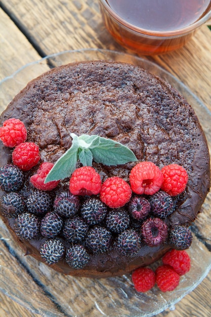 Zelfgemaakte chocoladetaart versierd met muntblaadjes zwarte en rode frambozen op glasplaat