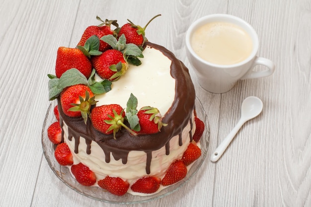 Zelfgemaakte chocoladetaart versierd met verse aardbeien op glasplaat en witte kop koffie