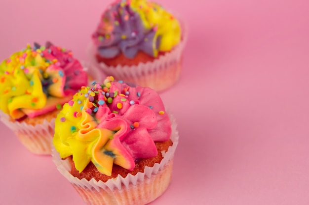 Zelfgemaakte cupcakes met veelkleurige crème op een roze achtergrond kopie ruimte. Geel en roze crème.