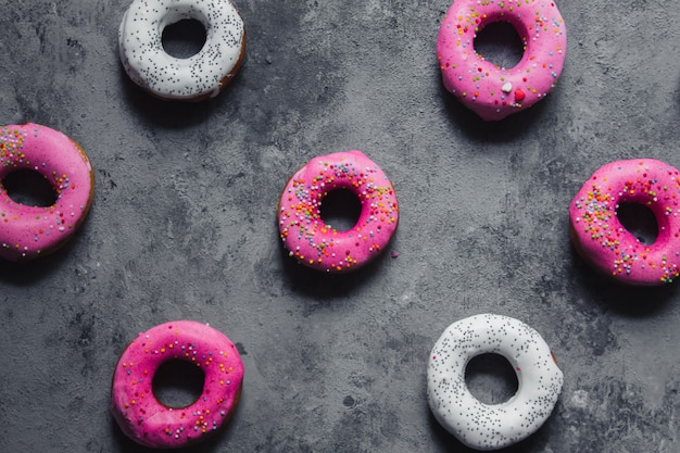 Zelfgemaakte donuts roze met regenboog hagelslag en wit met suikerglazuur maanzaad op het donkergrijs