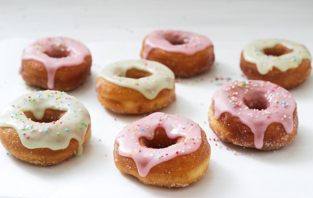 Zelfgemaakte donuts versierd met gekleurde suikerglazuur en gekleurde suiker op een lichte achtergrond.