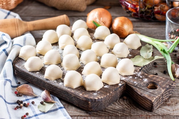 Zelfgemaakte dumplings met vlees op rustieke houten plank en tafel met bloem, horizontaal