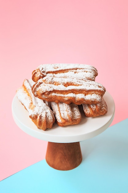 Zelfgemaakte eclairs met poedersuiker. Roomsoesjes gevuld vanillevla en bestrooid met suikerglazuur op een heldere achtergrond. Profiteroles met vanilleroom en poedersuiker.