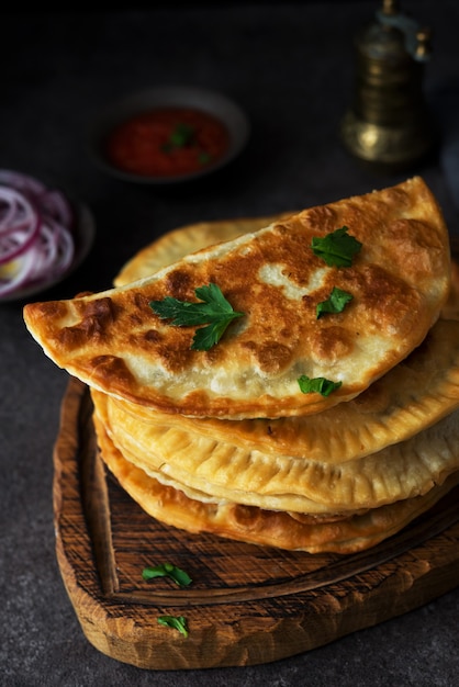 Zelfgemaakte gebakken empanadas met varkensvlees, chebureks met champignons op een houten bord